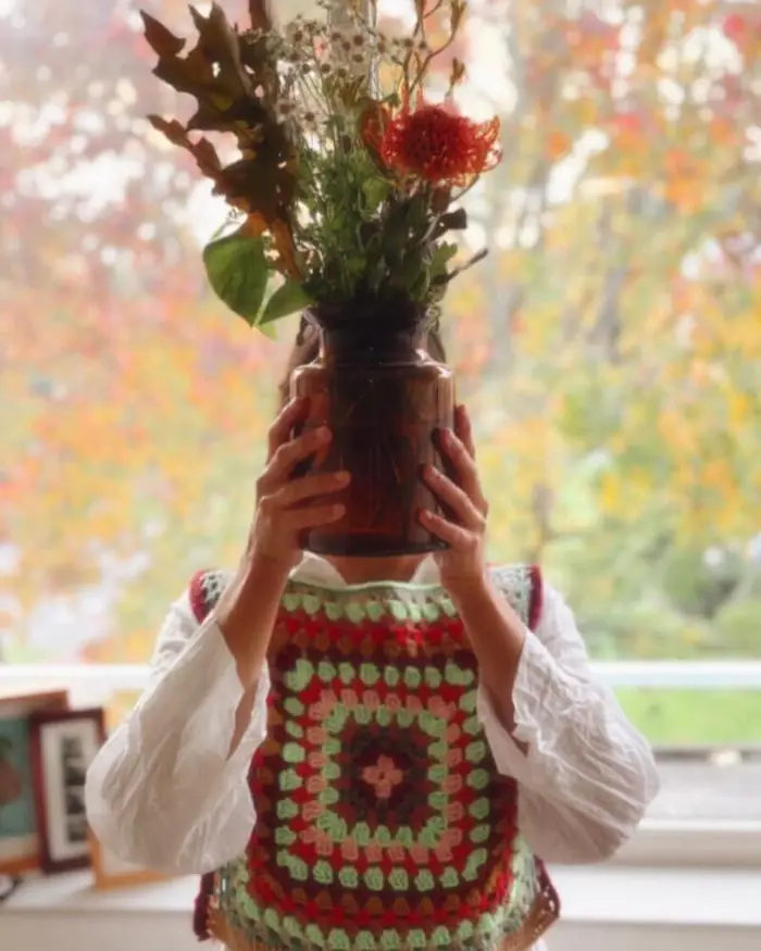 Crochet vest worn, holding a vase of dried flowers