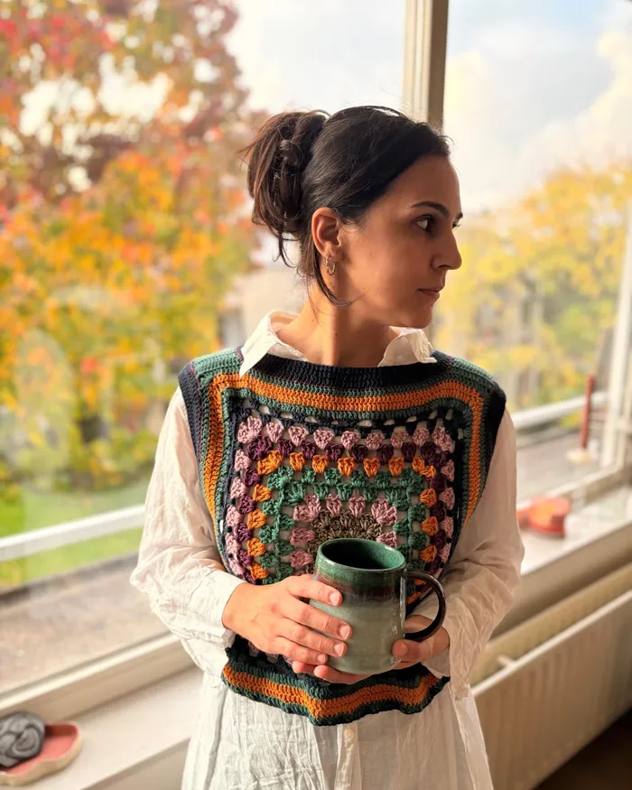 The Melina vest worn at a window, holding a mug